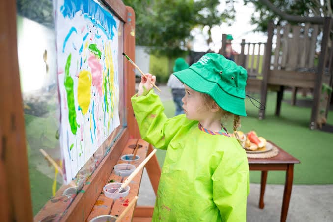 A child painting at an outdoor easel under a sunny sky