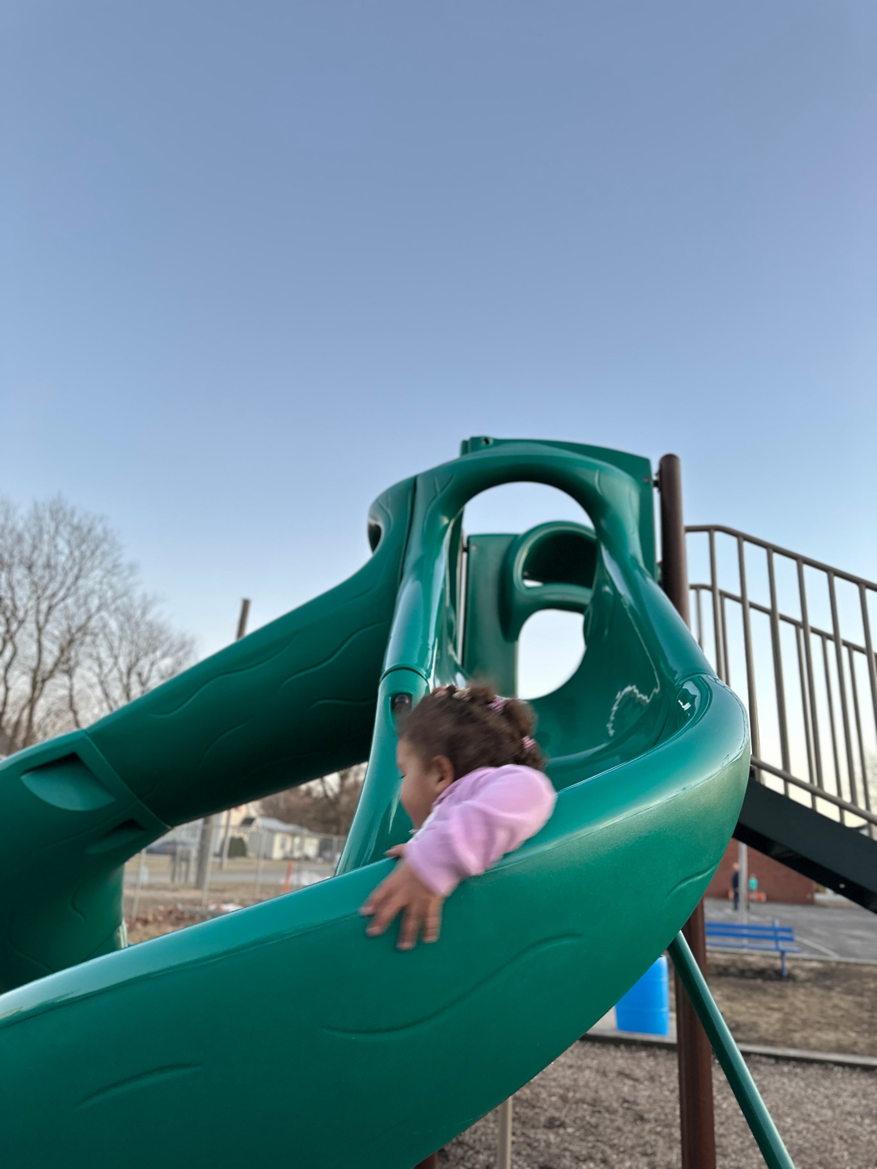 A toddler playing on a green playground slide